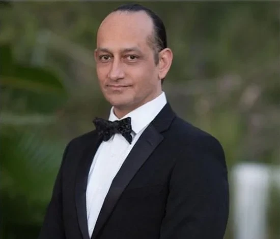 A man in a tuxedo posing for a photo at the Gynecomastia Surgery Insurance & Financing event.