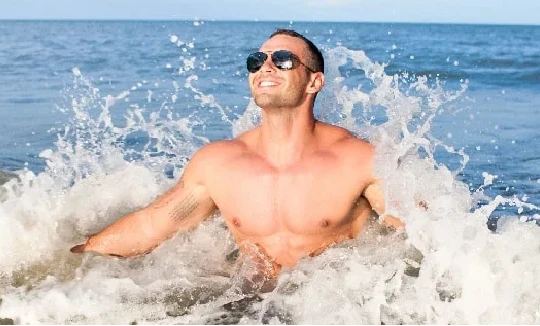 A man in sunglasses is splashing in the ocean.