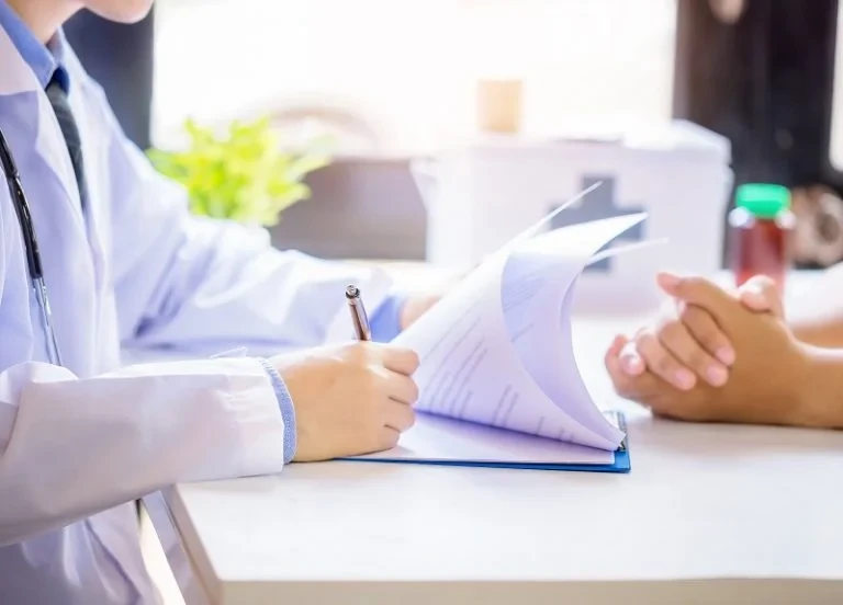 A doctor is discussing gynecomastia treatment with a patient at a desk.